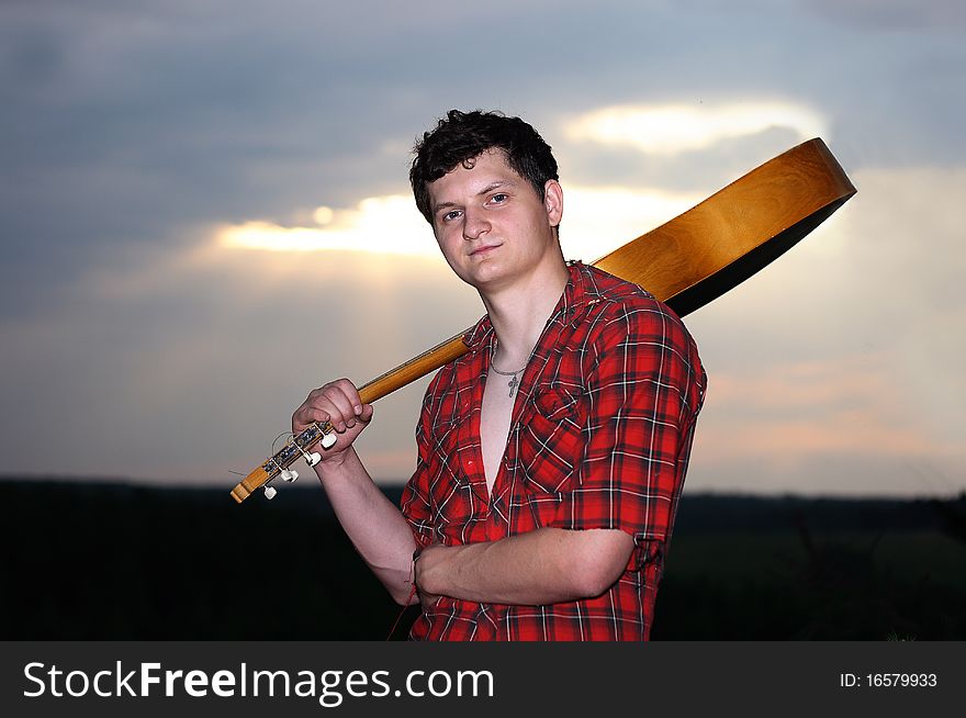 A young man with a guitar at sunset. A young man with a guitar at sunset