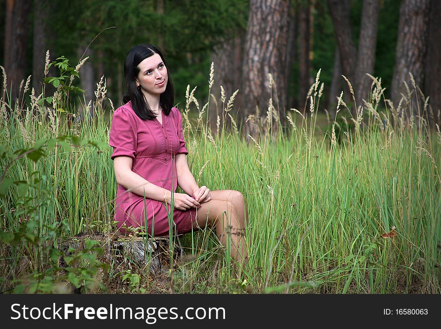 Girl in a red dress sitting on a stump in the woods. Girl in a red dress sitting on a stump in the woods