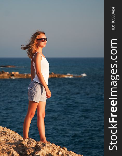 Beautiful young woman standing on a rock and looks at sea