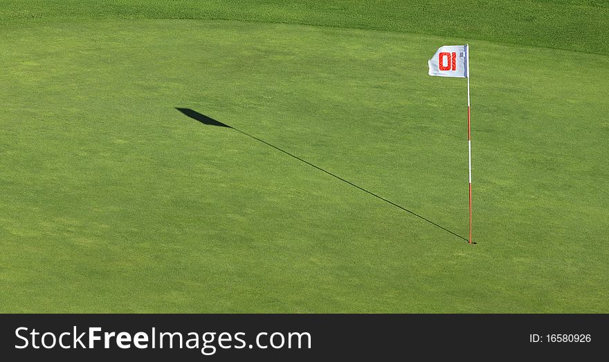 A flagpole and its shadow near the hole on a green golf field. A flagpole and its shadow near the hole on a green golf field.