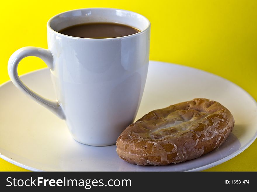 Coffee with honey bunn on plate with yellow background