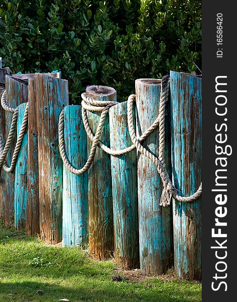 A large rope of the type used on a ship is draped over some blue fence posts in Hawaii. A large rope of the type used on a ship is draped over some blue fence posts in Hawaii.