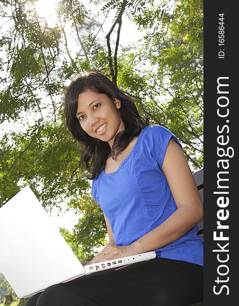 An Asian woman using her laptop on a park bench. An Asian woman using her laptop on a park bench