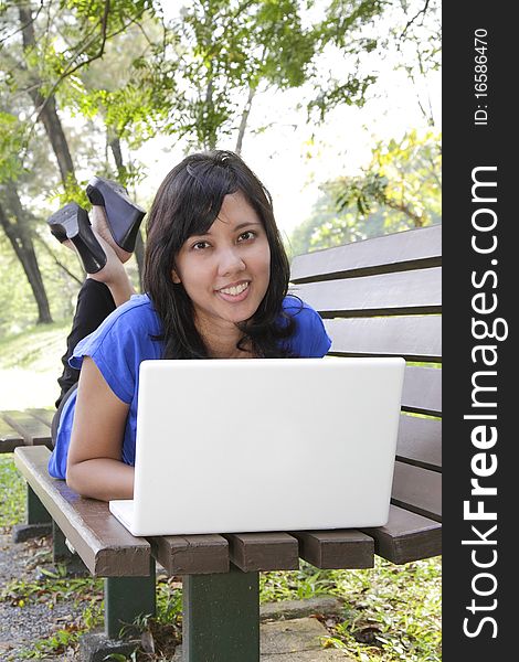 An Asian woman lying down on a bench using her laptop. An Asian woman lying down on a bench using her laptop