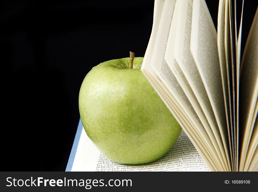 Green apple on an open book isolated on black