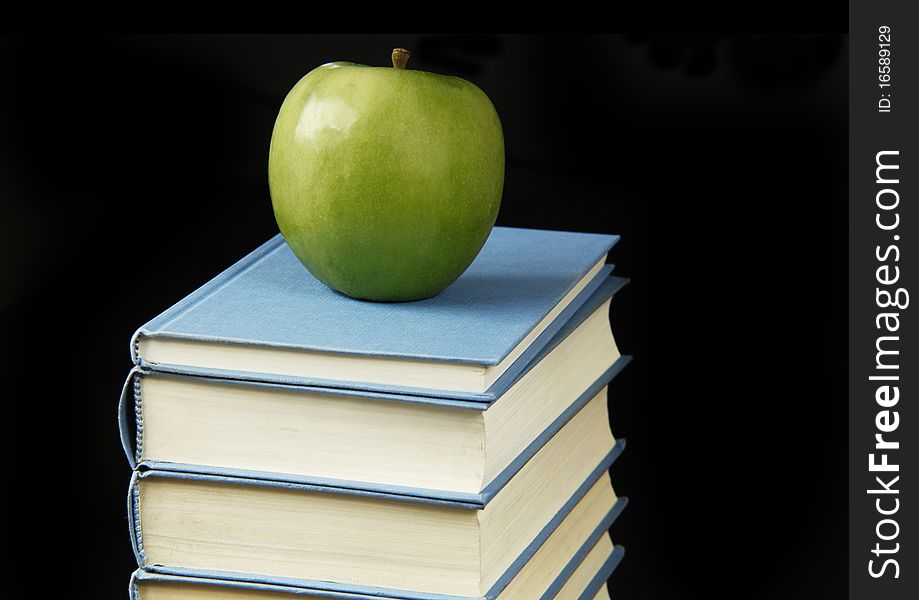 Green apple on on the stack of books isolated on black