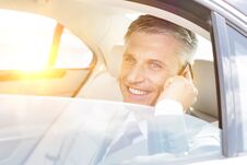 Smiling Mature Businessman Talking On Smartphone While Looking Through Window In Car With Yellow Lens Flare In Background Royalty Free Stock Images