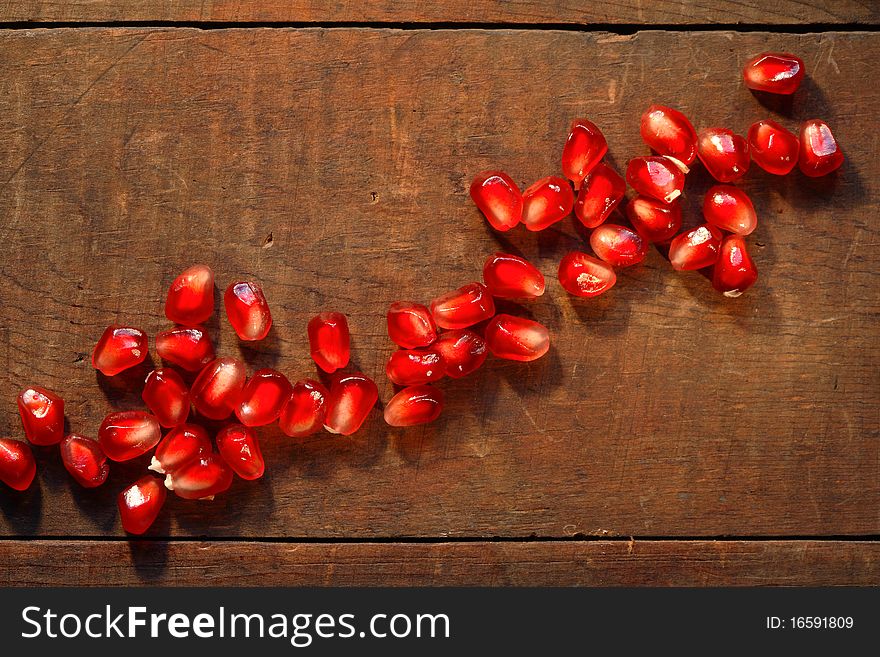 Lot of red pomegranate seeds lying in a row on dark wooden board
