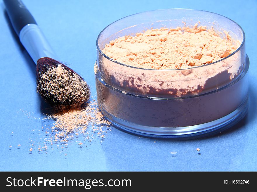 Loose powder on a blue background with the brush of natural bristles to apply it.