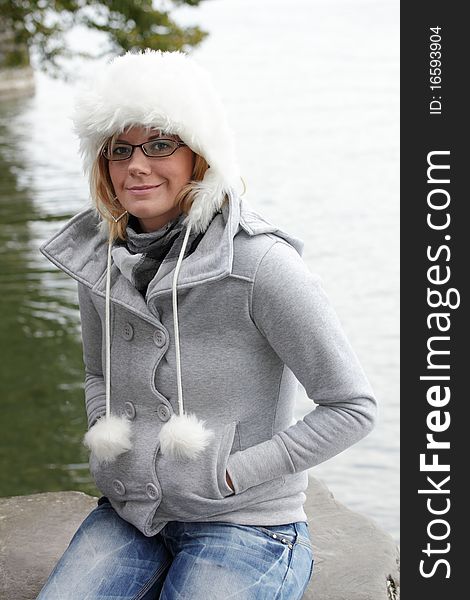 Young woman with white fur hat, smiling friendly looking into the camera. Autumn, monochrome mood at the lakeside. Young woman with white fur hat, smiling friendly looking into the camera. Autumn, monochrome mood at the lakeside.