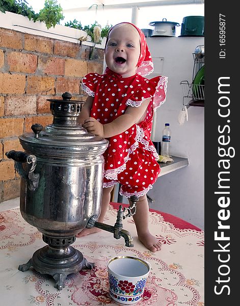 Little girl in a red polka-dot dress, with a samovar, stand in front of a brick wall and smiling. Little girl in a red polka-dot dress, with a samovar, stand in front of a brick wall and smiling.