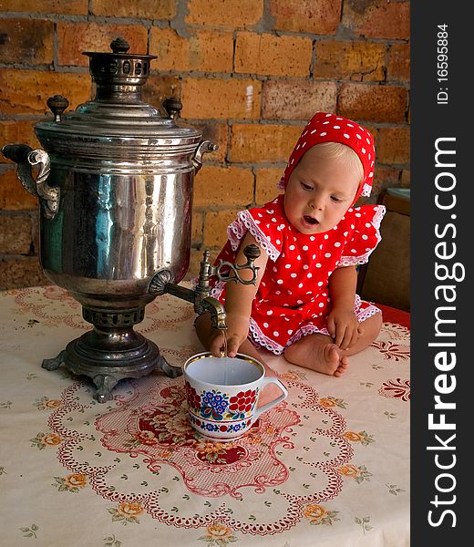 Little girl in a red polka-dot dress, with a samovar, sitting in front of a brick wall and pours water into a cup. Little girl in a red polka-dot dress, with a samovar, sitting in front of a brick wall and pours water into a cup