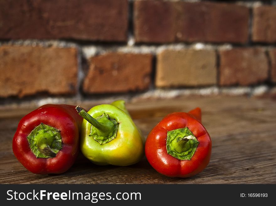 Three peppers on a wooden table with a red wall in the background.