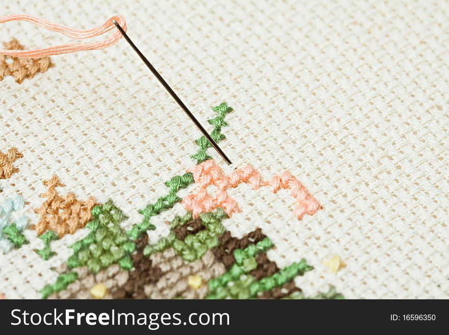 Closeup of needle put into cross-stitch embroidery.