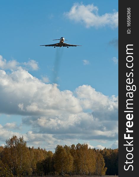 The photograph shows the aircraft, preparing to sit down at the airport. Frame is made against the backdrop of autumn forest and clouds. The photograph shows the aircraft, preparing to sit down at the airport. Frame is made against the backdrop of autumn forest and clouds.