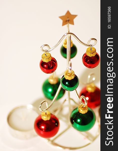 Close up of a wire Christmas tree with red and green ornaments on a white background.