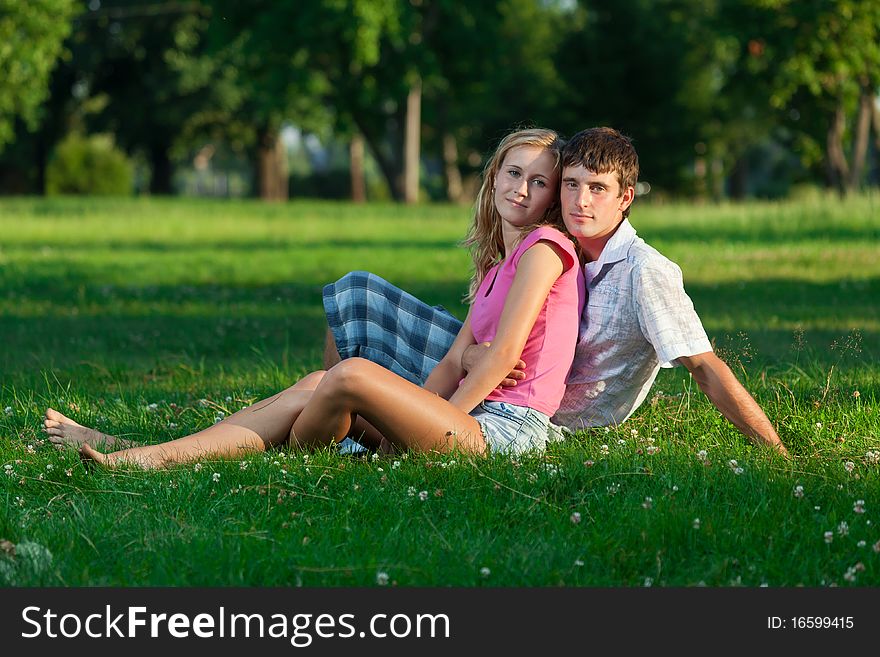 Two young lovers sitting on the lawn in the park and looks into the camera