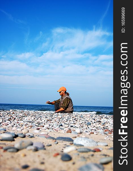 A man sitting on a rocky beach in early autumn.