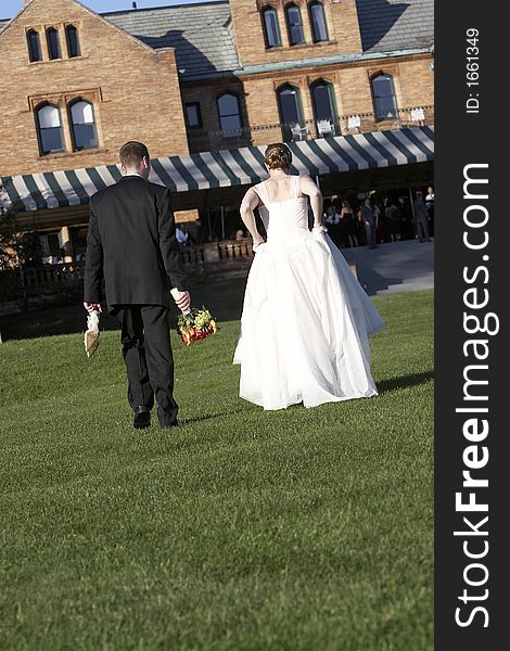 A bride and groom walking away from the camera. He is holding her shoes. A bride and groom walking away from the camera. He is holding her shoes