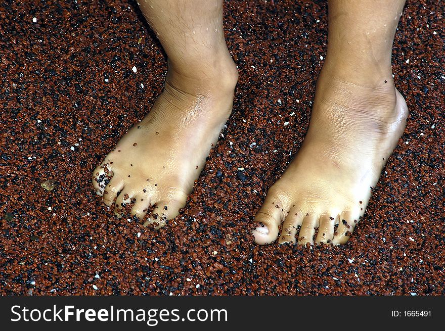 Wet feet of a kid on a red sand beach