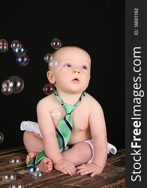 Cute baby boy sitting on an antique trunk looking at bubbles. Cute baby boy sitting on an antique trunk looking at bubbles