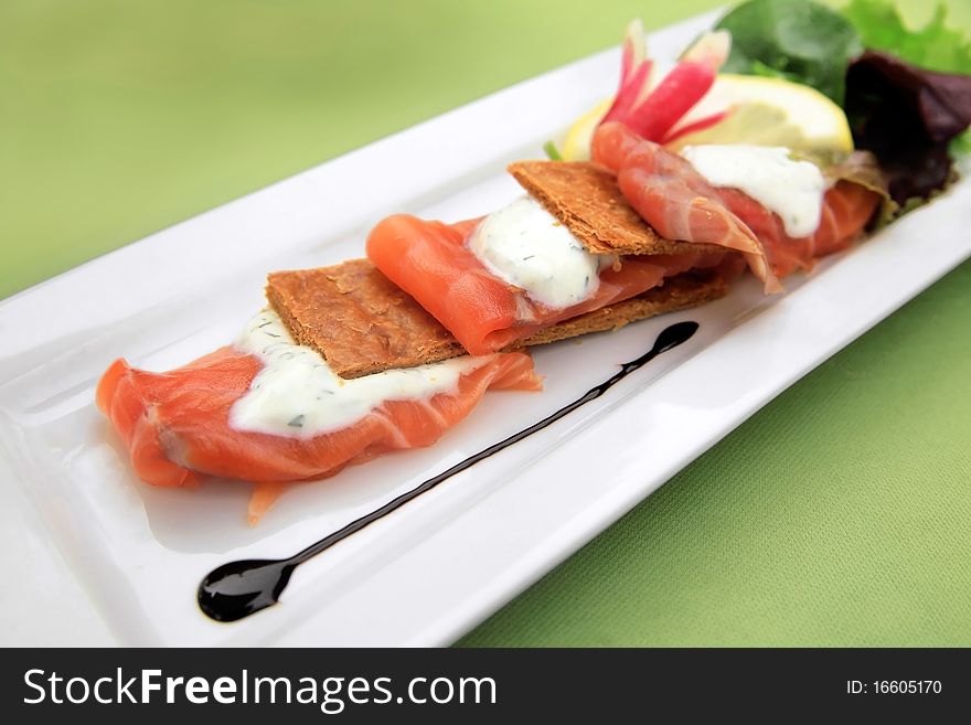 Smoked salmon slices on puff pastry with seasoned cream. Served here with mixed salad and slice of lemon.