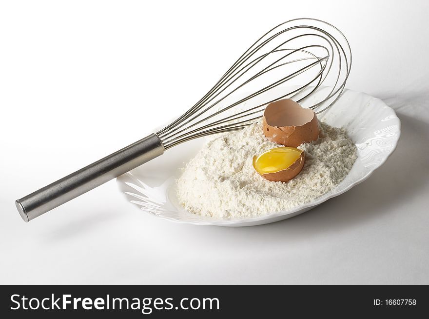 Flour pile, egg and metal whisker over gray gradient background. Flour pile, egg and metal whisker over gray gradient background