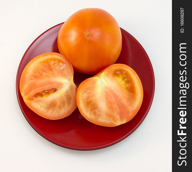 One whole tomato and the two halves lying on a brown plate. One whole tomato and the two halves lying on a brown plate.