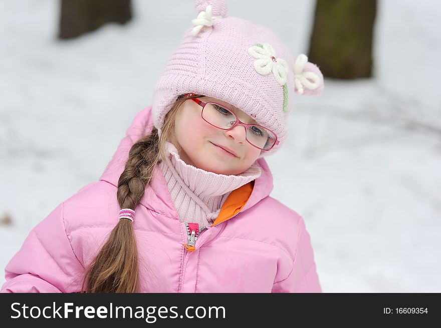 Adorable winter small girl in glasses and pink hat and jacket in the forest