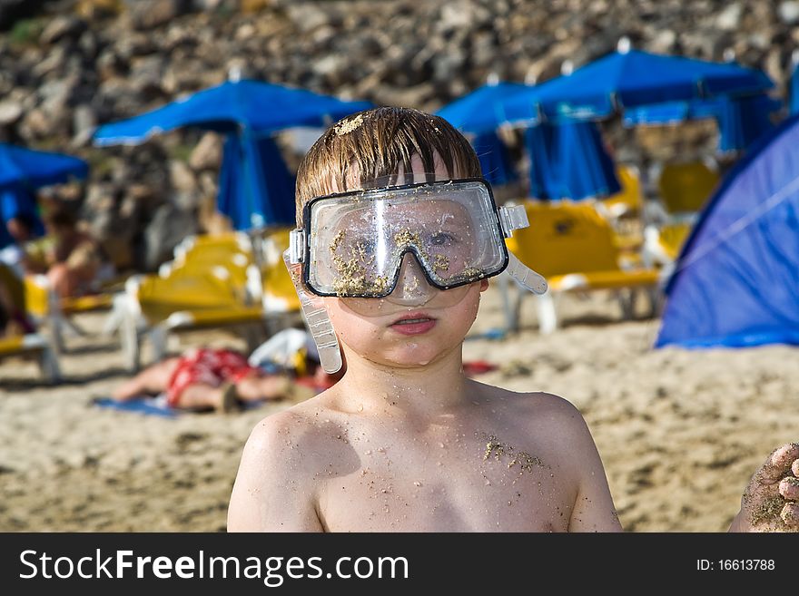 Child, boy with diving goggles at the sandy beach