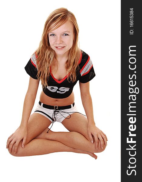 A young teenage soccer girl sitting on the floor in her uniform, with her legs crossed, for a portrait in the studio, over white background. A young teenage soccer girl sitting on the floor in her uniform, with her legs crossed, for a portrait in the studio, over white background.