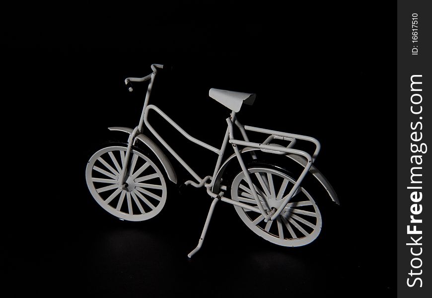 A white metal miniature bike on a black background, a little worn object. A white metal miniature bike on a black background, a little worn object