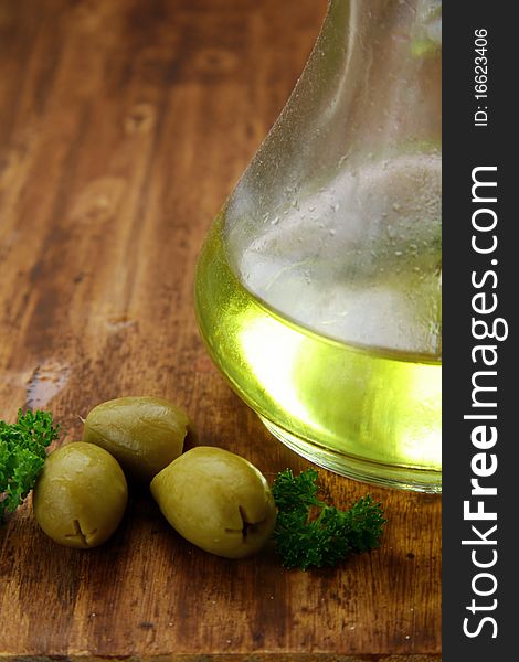 Bottle with olive oil and green olives on a wooden board