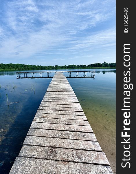 Wooden pontoon on a lake with forest opposite and blue sky above