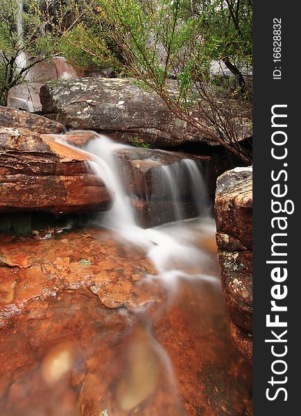 A creek cascades over some typically australian red rock. A creek cascades over some typically australian red rock
