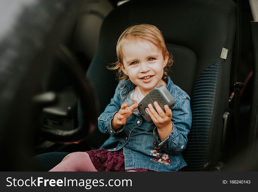 Little girl in a car seat. Holding phone in her hand. Taking driver seat. Car damage. Authentic image