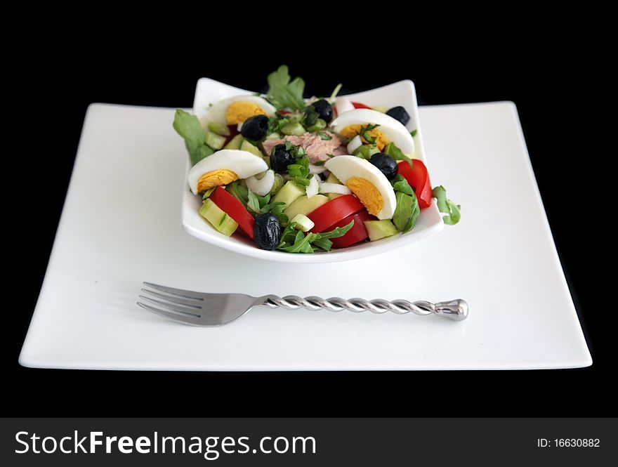 Niçoise salad (without the anchioves & peppers) on white plate shot on black background.