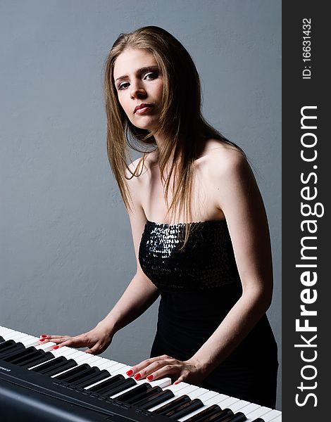 Beautiful girl in black dress playing on keyboard. Beautiful girl in black dress playing on keyboard