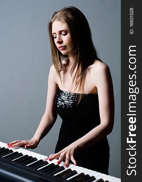 Beautiful girl in black dress playing on keyboard. Beautiful girl in black dress playing on keyboard