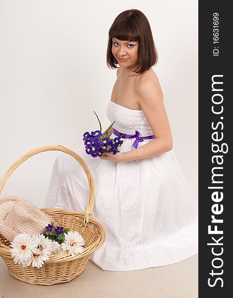 Beautiful girl holding a bouquet of irises and a basket, which is a hat and a bouquet of white flowers. She is in studio isolated on a white background. Beautiful girl holding a bouquet of irises and a basket, which is a hat and a bouquet of white flowers. She is in studio isolated on a white background
