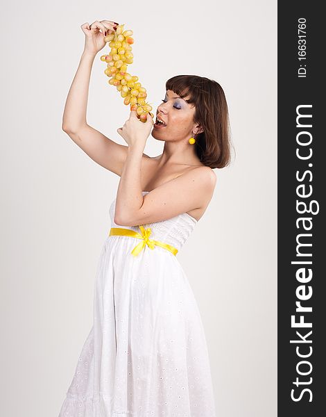 Beautiful girl in white dress with yellow tape is holding green grapes. She is isolated on a white background. Beautiful girl in white dress with yellow tape is holding green grapes. She is isolated on a white background.