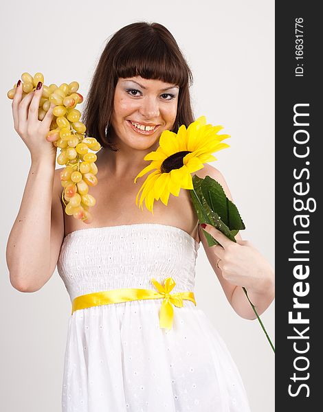 Beautiful girl in white dress with yellow tape is holding green grapes and sunflower. She is isolated on a white background. Beautiful girl in white dress with yellow tape is holding green grapes and sunflower. She is isolated on a white background.