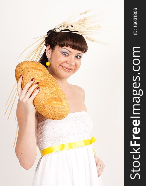 Beautiful brunette girl with ears of wheat in her hair is eating a bread isolated on the white background. Beautiful brunette girl with ears of wheat in her hair is eating a bread isolated on the white background