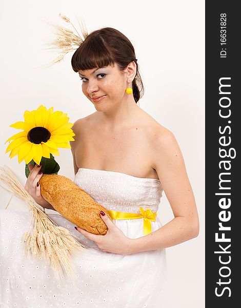 Beautiful brunette girl with sunflower and ears of wheat in her hair is eating a bread isolated on the white background. Beautiful brunette girl with sunflower and ears of wheat in her hair is eating a bread isolated on the white background