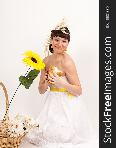 Beautiful brunette girl with sunflower and ears of wheat in her hair is eating a bread isolated on the white background. Beautiful brunette girl with sunflower and ears of wheat in her hair is eating a bread isolated on the white background