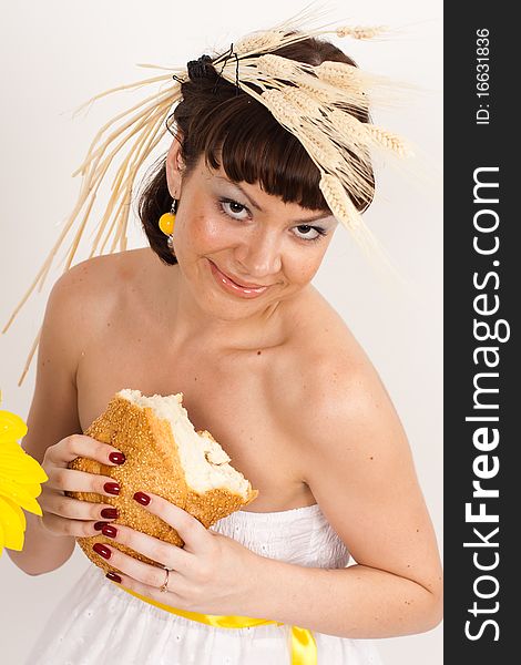 Beautiful brunette girl with ears of wheat in her hair is eating a bread isolated on the white background. Beautiful brunette girl with ears of wheat in her hair is eating a bread isolated on the white background