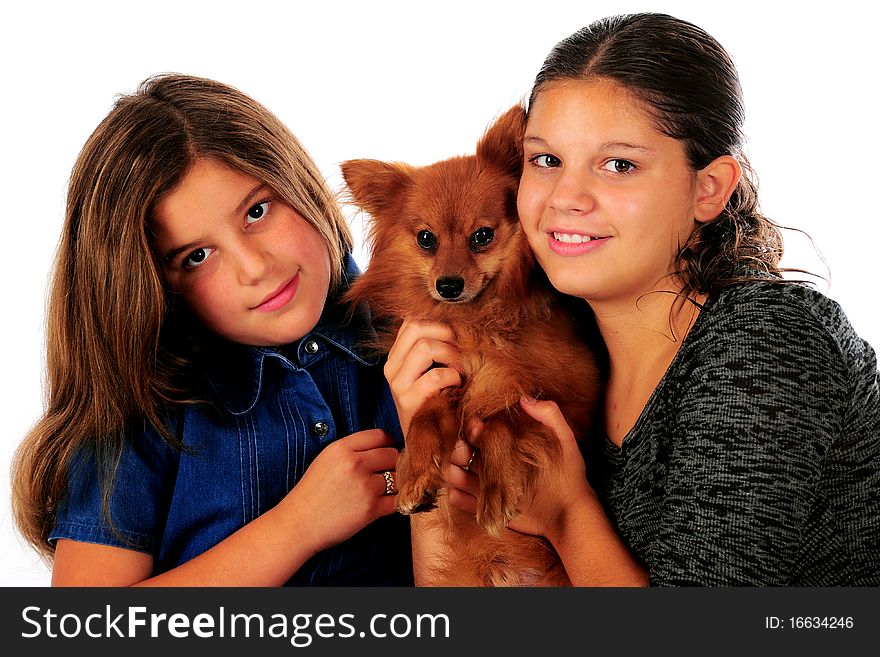 A young teen and her preteen sister loving on a Pomeranian puppy. Isolated on white. A young teen and her preteen sister loving on a Pomeranian puppy. Isolated on white.