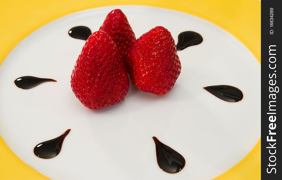Three strawberries decorated with chocolate drops on a porcelain plate. Three strawberries decorated with chocolate drops on a porcelain plate