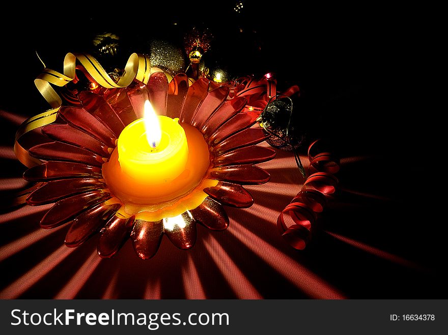 A red glass candlestick with a burning candle and Xmas adornments. A red glass candlestick with a burning candle and Xmas adornments.