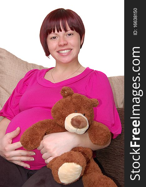 Happy young pregnant woman sitting on the sofa with teddy